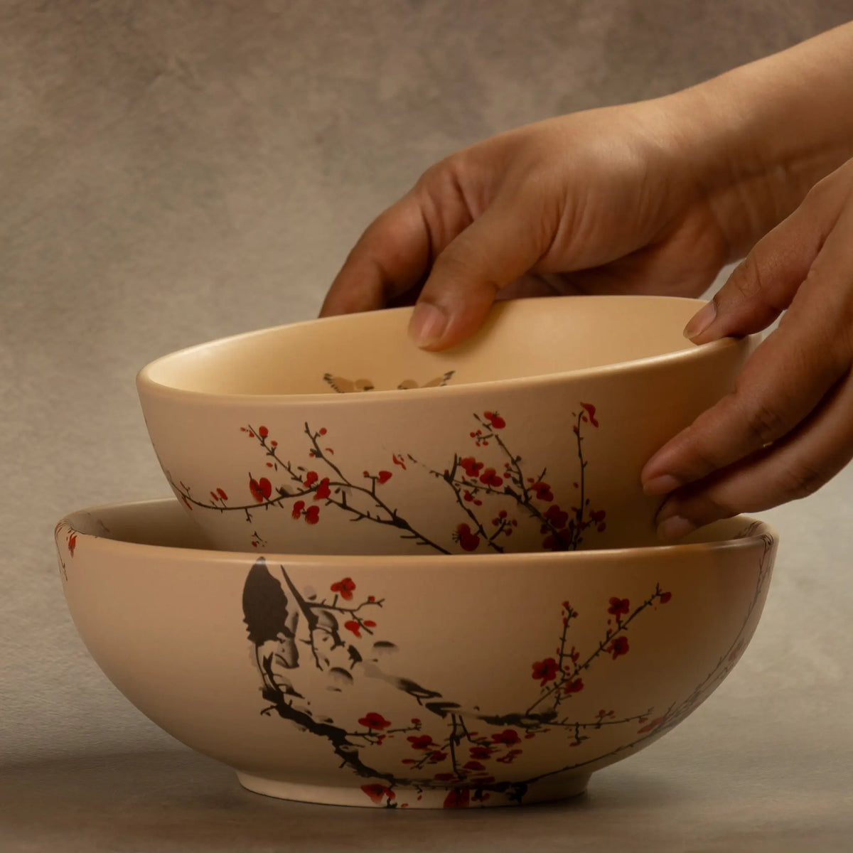 Hands stacking Sakura salad bowls with cherry blossom design