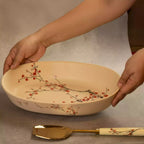 Hands holding Sakura baking dish with brass serving spoon