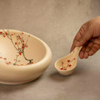 Hand holding ceramic spoon over Sakura nest platter with blossom design