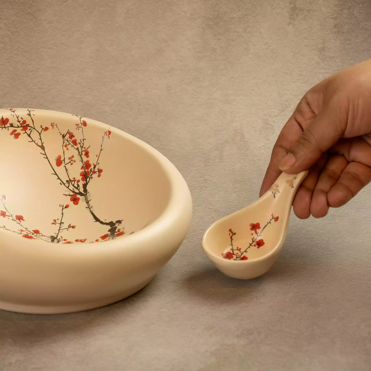 Hand holding ceramic spoon over Sakura nest platter with blossom design