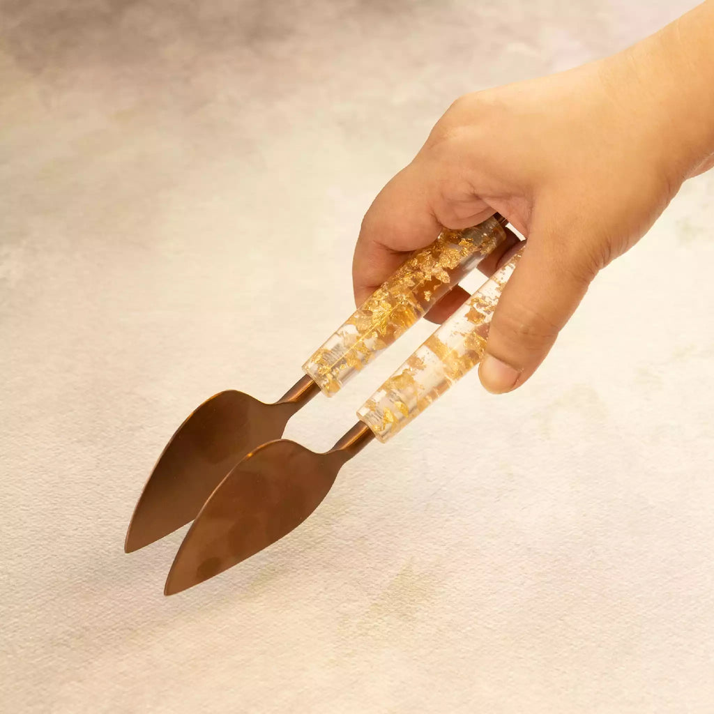 Hand holding gold dust serving tongs with resin handle