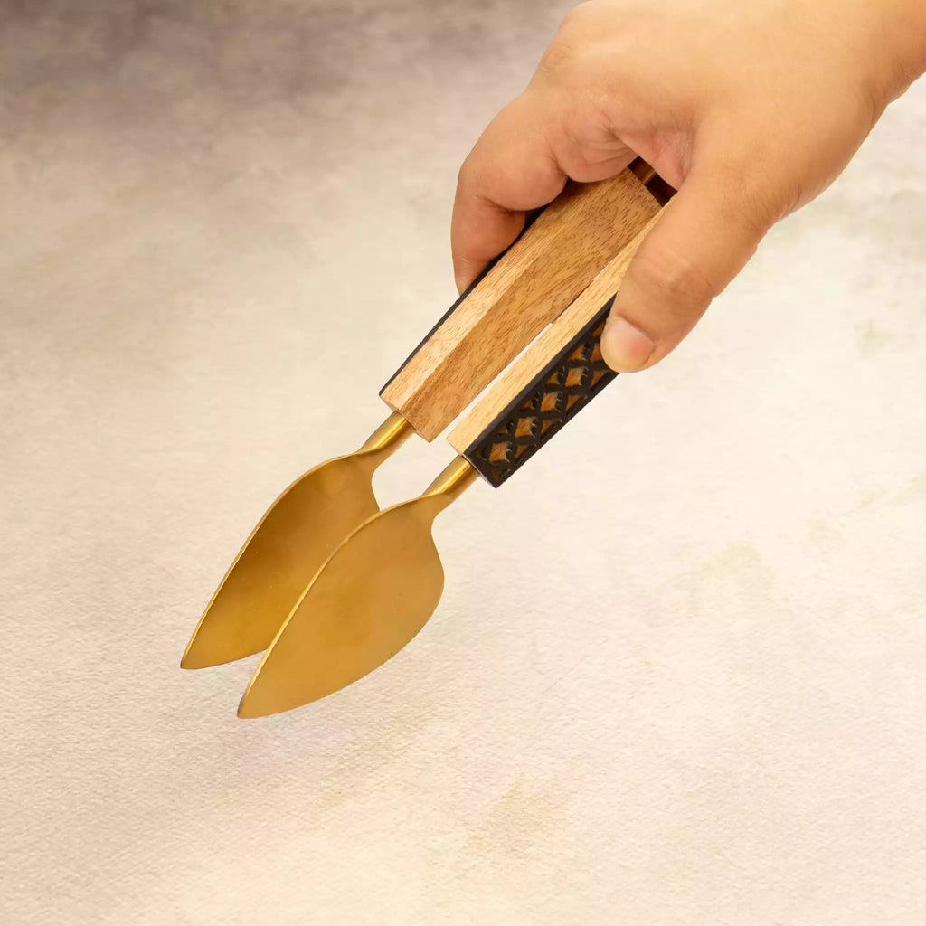 Hand holding carved brass serving tongs from spatula trio