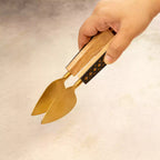 Hand holding carved brass serving tongs from spatula trio