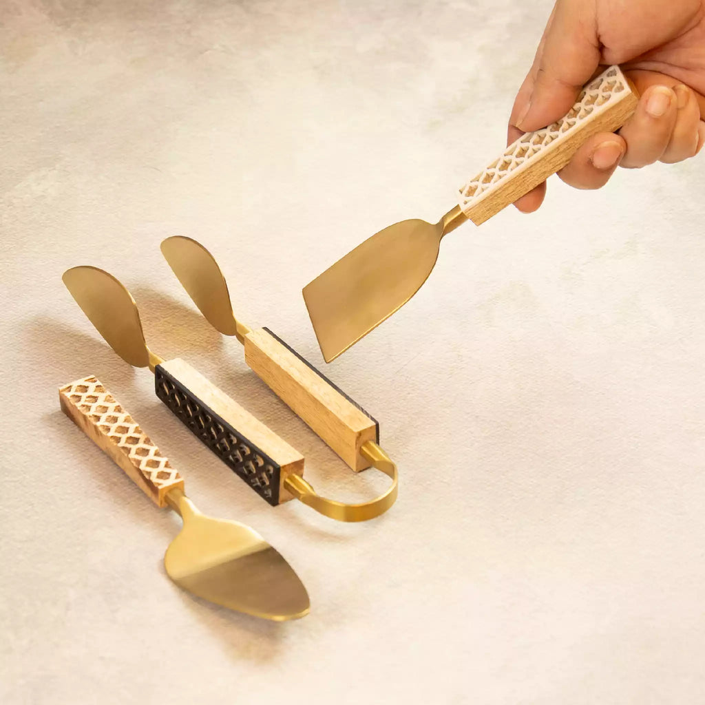Hand holding carved brass tongs above spatula trio set