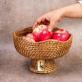 Hand placing apples in cane fruit bowl with pedestal