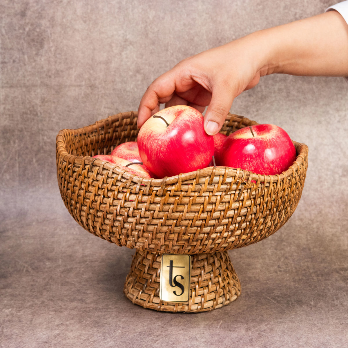 Hand placing apples in cane fruit bowl with pedestal