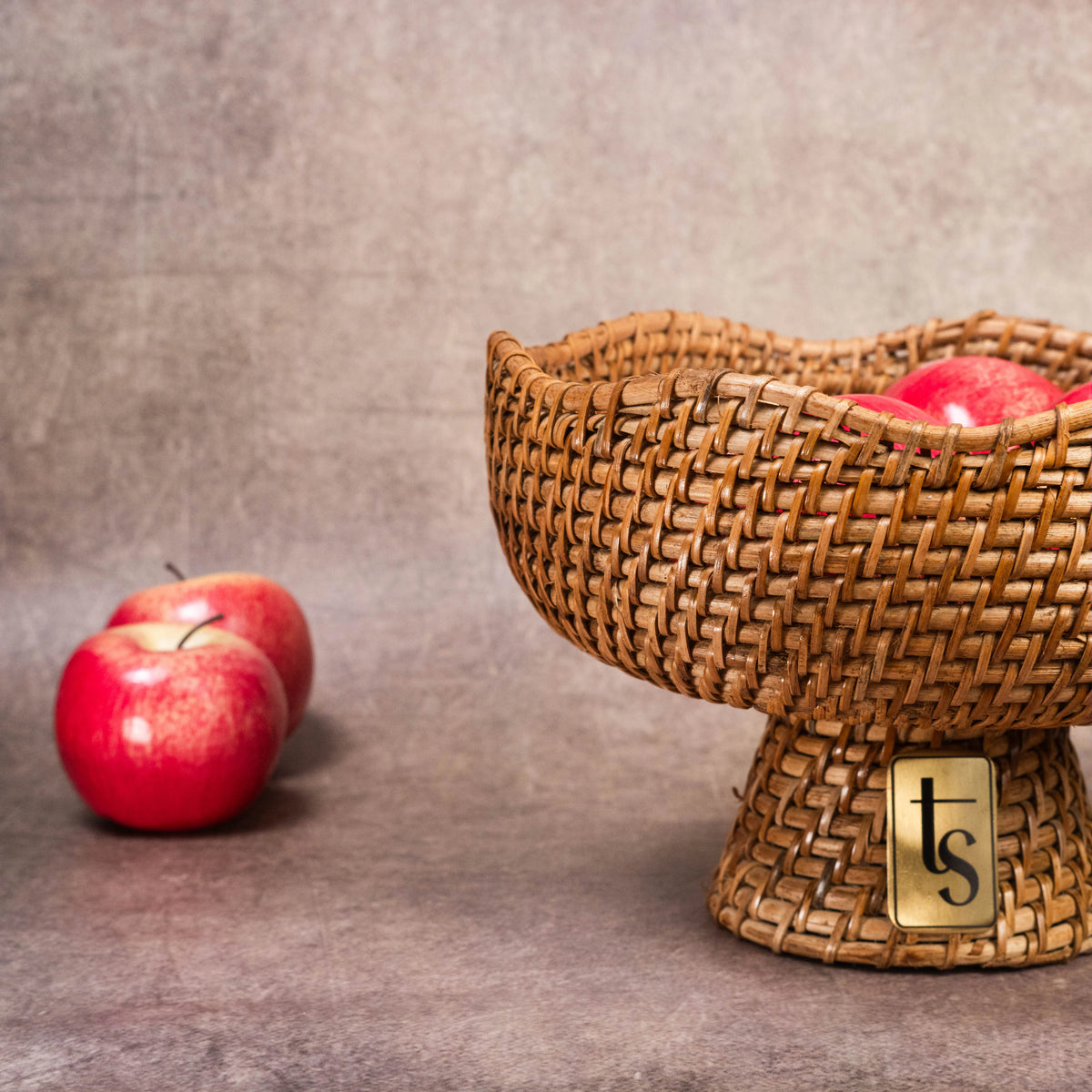 Cane fruit bowl with red apples beside on grey backdrop